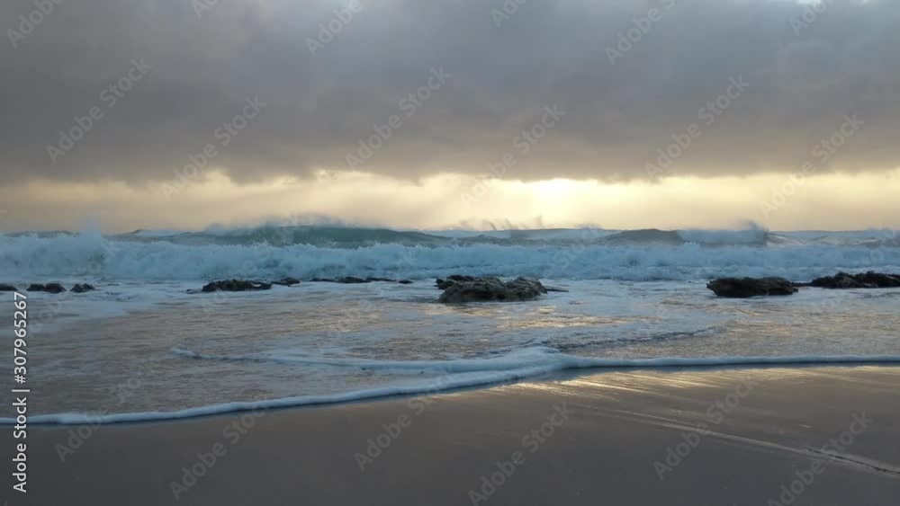 Waves gently washing and crashing across large rocks on a beach during sunrise Waves gently washing and crashing across large rocks on a beach during sunrise