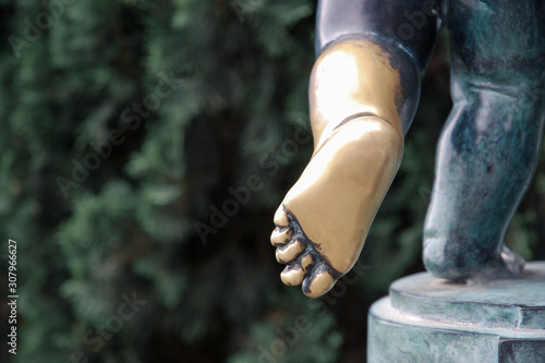 Part of an old oxidized bronze statue of a child with a polished leg and foot. Achilles heel, metaphor for vulnerability or weakness