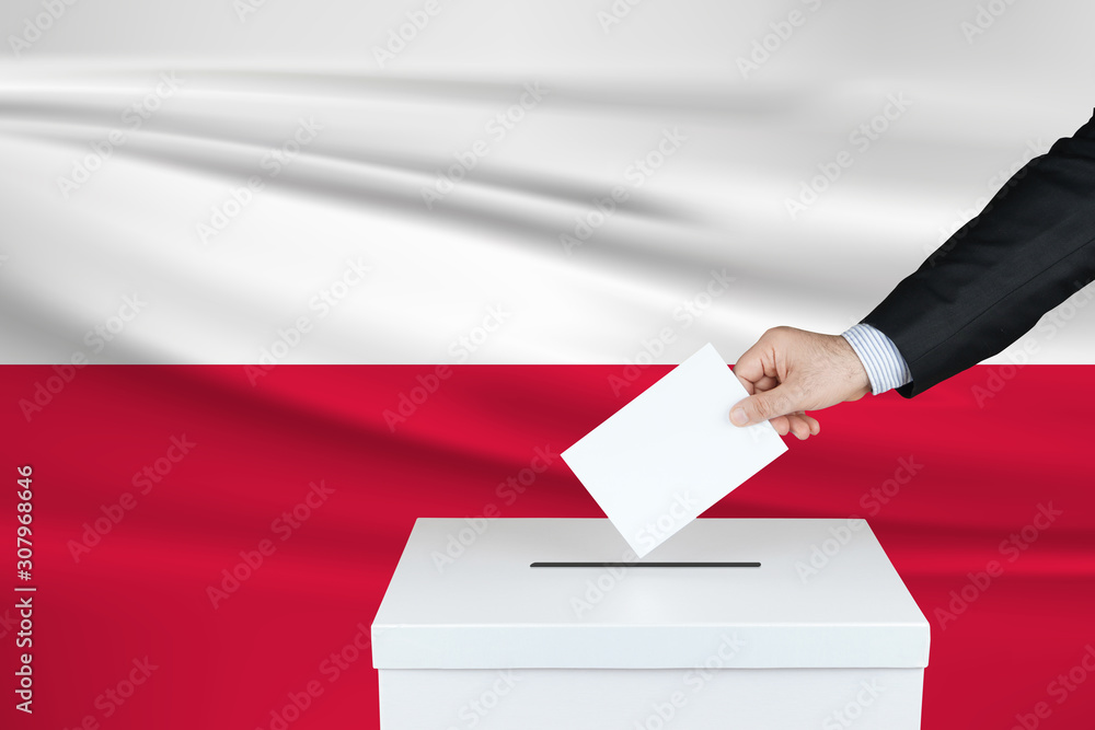 Election in Poland. The hand of man putting his vote in the ballot box. Waved Poland flag on background. Election in Poland. The hand of man putting his vote in the ballot box. Waved Poland flag on background.