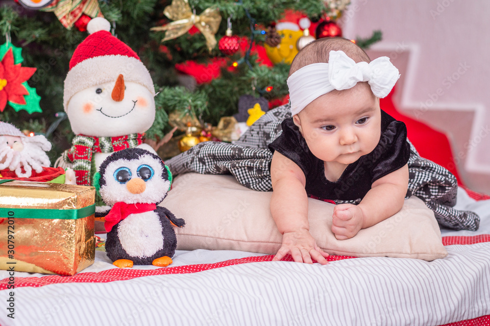 A white baby in Christmas tree decoration with black dress and white bow, on the cushion looks out A white baby in Christmas tree decoration with black dress and white bow, on the cushion looks out