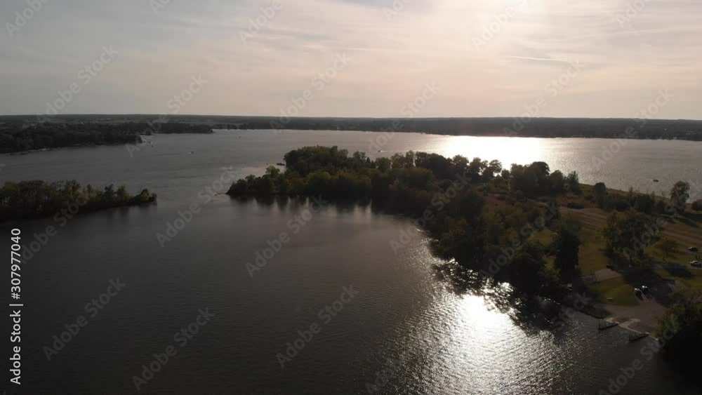 Golden sunset over the surface of the water with a bright wake that is drawn between the surface waves, number of trees can be seen on ground surfaces Golden sunset over the surface of the water with a bright wake that is drawn between the surface waves, number of trees can be seen on ground surfaces