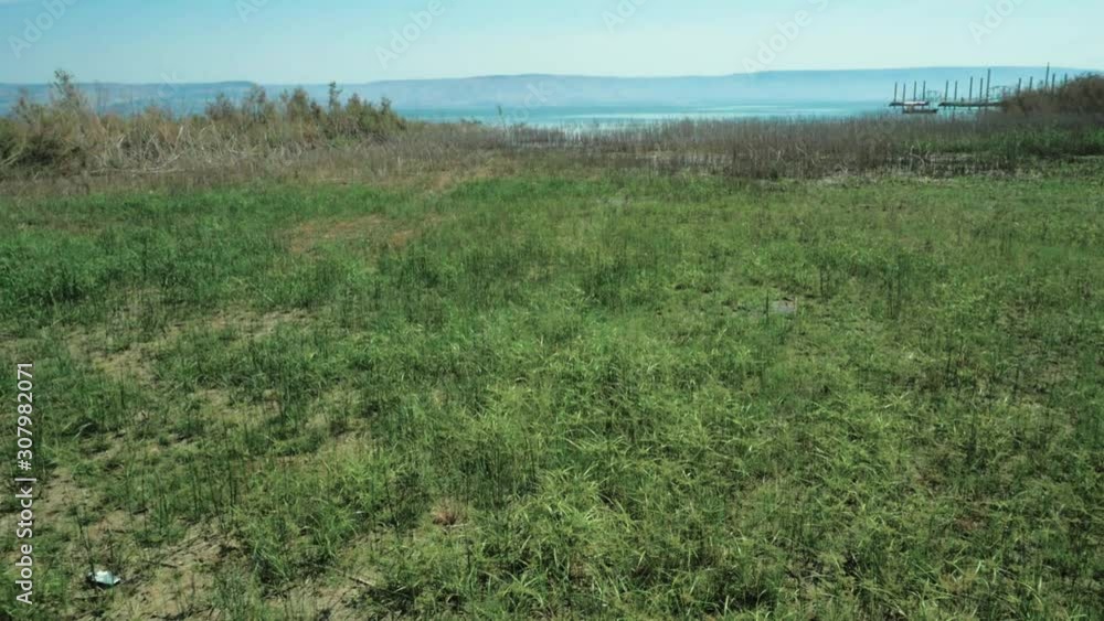 Slow dolly/pan over grass field, historical sea of galillee in background