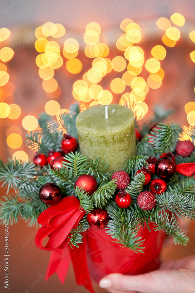 Small arrangement of fresh spruce with a candle in a ceramic pot. Christmas mood. Bokeh of Garland lights on background.