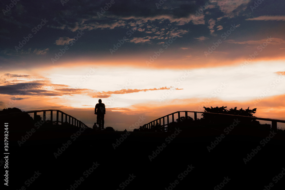 Silhouette of active people on pedestrian bridge against low sunset