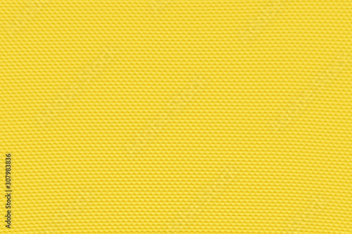 Golden yellow background from a textile material with pattern, closeup. Structure of banana yellow fabric with punching texture. Perforated cloth backdrop.