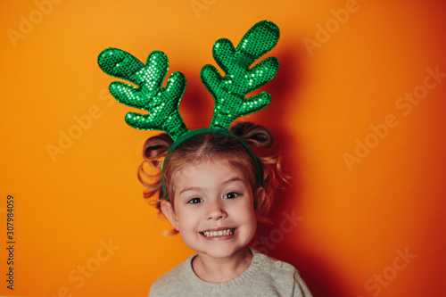 Christmas card with copy space. Happy kid with green christmas antlers on head. A kid with healthy while teeth is smiling.