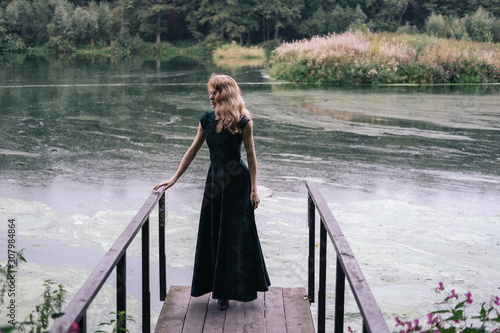 Portrait of fashion female wearing Hollywood wave hair style and long dress, standing on the bridge near beautiful dirty pond © Annatamila