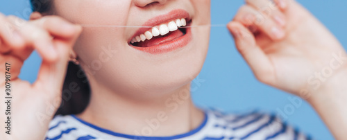 Fototapeta Naklejka Na Ścianę i Meble -  Happy smiling woman with white perfect teeth flossing, dental floss on blue background, clode up photo.