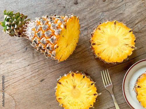 Ripe pineapple slice is served with plate, knife and fork on the wooden table.