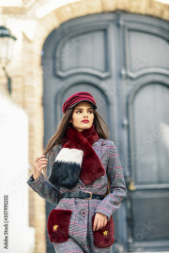 Young beautiful girl with very long hair looking away wearing winter coat and cap outdoors.