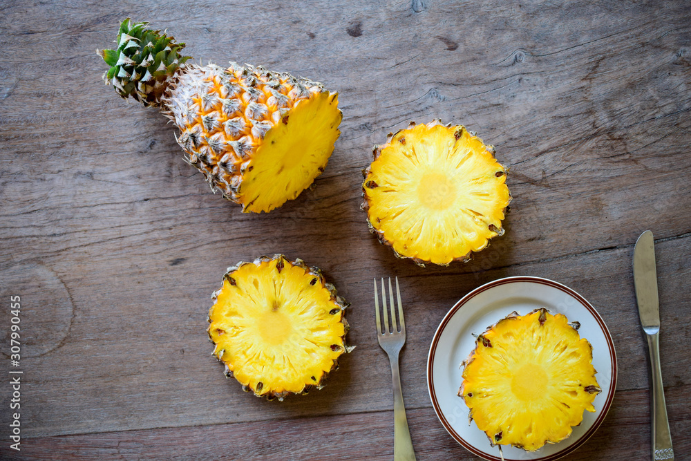 Ripe pineapple slice is served with plate, knife and fork on the wooden table. Ripe pineapple slice is served with plate, knife and fork on the wooden table.