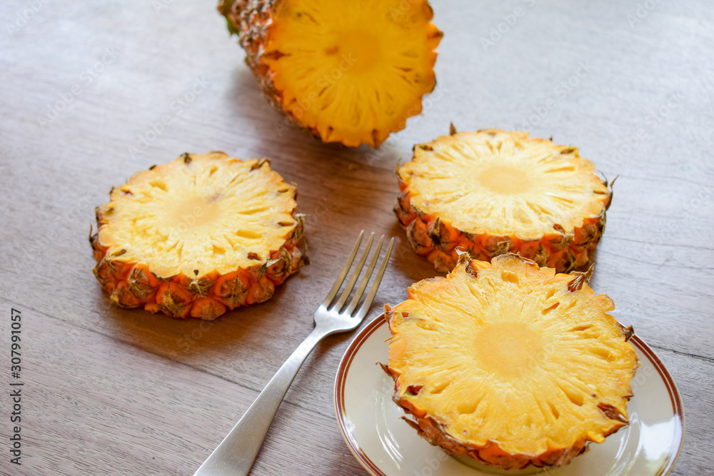 Ripe pineapple slice is served with plate, knife and fork on the wooden table. Ripe pineapple slice is served with plate, knife and fork on the wooden table.