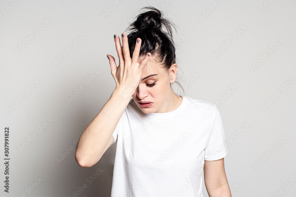 Young woman suffers from a severe headache. She pressed her hand to her forehead, looking down and wants to cry. Health concept. Young woman suffers from a severe headache. She pressed her hand to her forehead, looking down and wants to cry. Health concept.