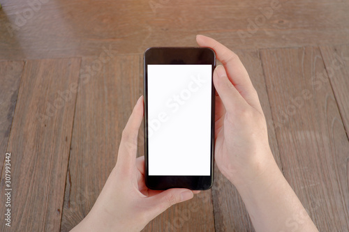 Mockup picture of human’s hands holding smart phone with white blank screen in modern place.