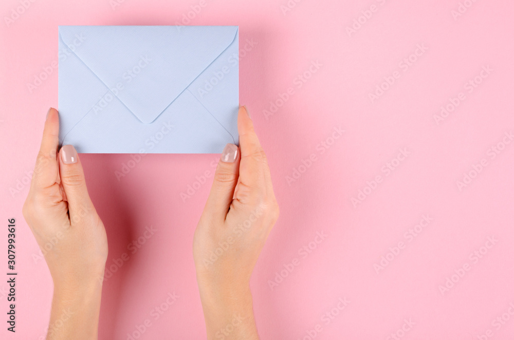 Hand with blue paper envelope composition on pink background.