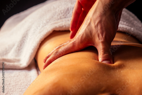 Masseur hands doing back massage to client in spa center in dark room
