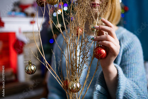 The girl touches the hand of a dry plant on which the Christmas tree toys are hung