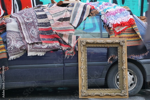 Fototapeta Naklejka Na Ścianę i Meble -  A car packed with rugs and a propped up picture frame at a street market in Athens