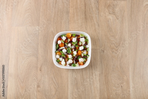 Mediterranean salad with fresh vegetables in a withe bowel on a wooden background