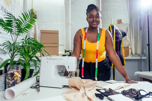 Young african american dressmaker woman sews clothes on sewing machine at tailor office it tropical summer style photo