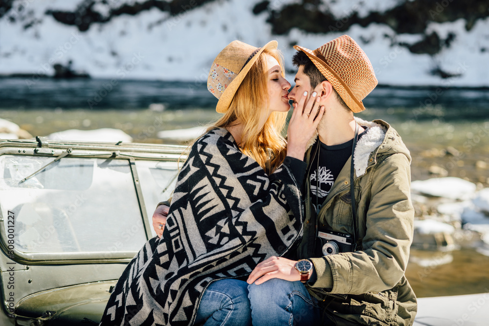 Beautiful young couple have fun and kisses near their car at winter mountains
