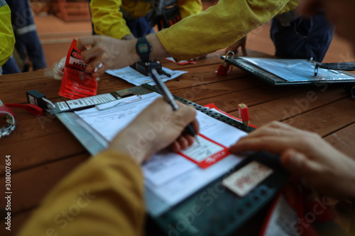 Defocused of construction miners worker hand holding pencil writing name and sign on personnel red danger tag prior placing locking into safety isolation permit control lock box 