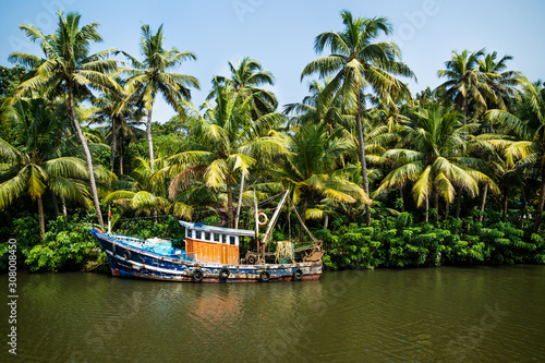Old ocean fishing boat along the canal Kerala backwaters shore with palm trees between Alappuzha and Kollam, India