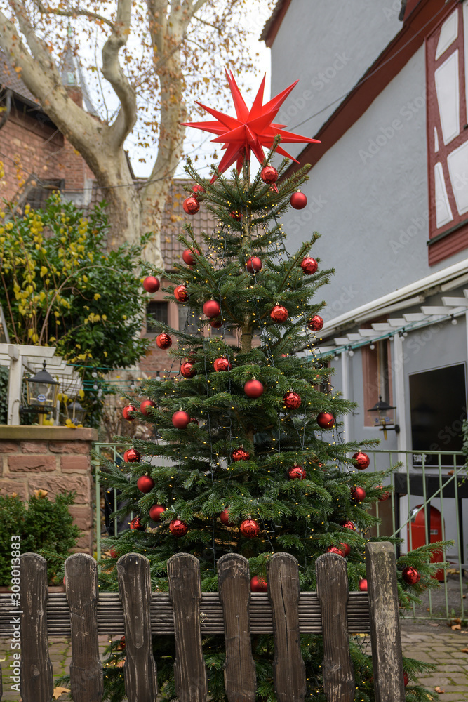 Christmas tree decorated with red balls and a chain of lights outdoors in an old town alley in Aschaffenburg, Bavaria, Germany