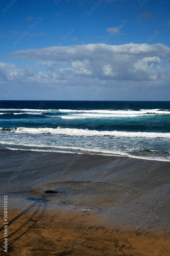 Playa de arena con ondas del agua a partir de una piedra y cielo con nubes