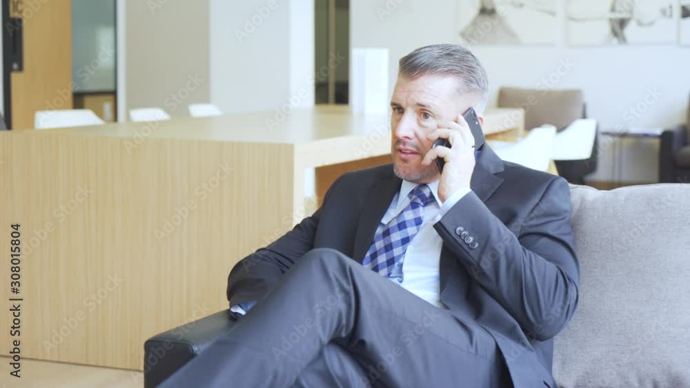 Caucasian businessman talking on mobile phone while sitting on the sofa in the office lobby. Shot in 4k resolution Caucasian businessman talking on mobile phone while sitting on the sofa in the office lobby. Shot in 4k resolution