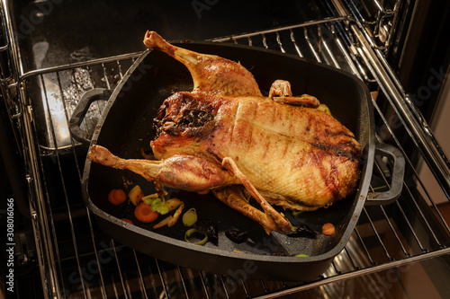 Whole duck roasted in a black pan on a grid in the oven for a festive Christmas menu, selected focus
