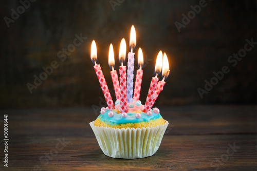 birthday muffin or cupcake with red and blue burning candles on a rustic wooden board against a dark brown background, copy space, selected focus, narrow depth of field