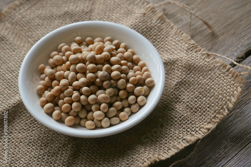 Soybeans in a white plate on rug sack on wooden background. 