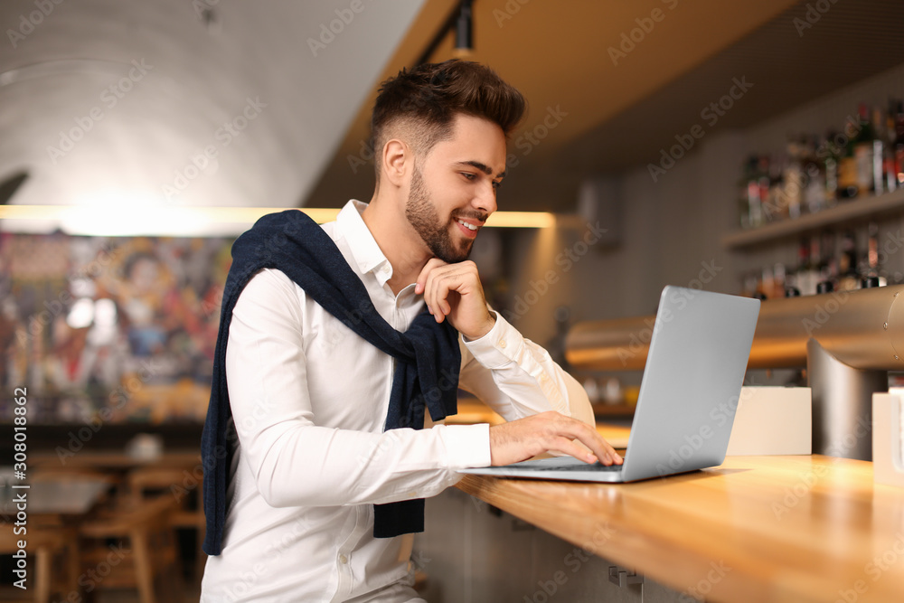 Young male business owner working with laptop at counter in his cafe