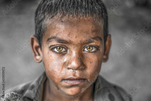 closeup of a poor staring hungry orphan boy in a refugee camp with sad expression on his face and his face and clothes are dirty and his eyes are full of pain