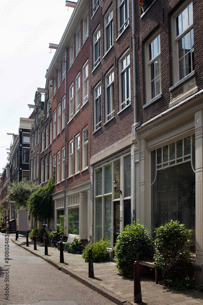 View of historical, typical and traditional buildings showing Dutch architectural style in Jordaan neighborhood and plants, flowers in Amsterdam. It is a sunny summer day. View of historical, typical and traditional buildings showing Dutch architectural style in Jordaan neighborhood and plants, flowers in Amsterdam. It is a sunny summer day.