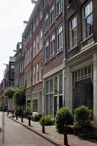 View of historical, typical and traditional buildings showing Dutch architectural style in Jordaan neighborhood and plants, flowers in Amsterdam. It is a sunny summer day.