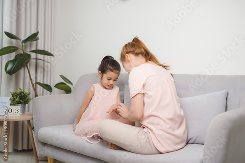 mom using pink nail polish to paint her cute daughter's nail to make her happier and prettier