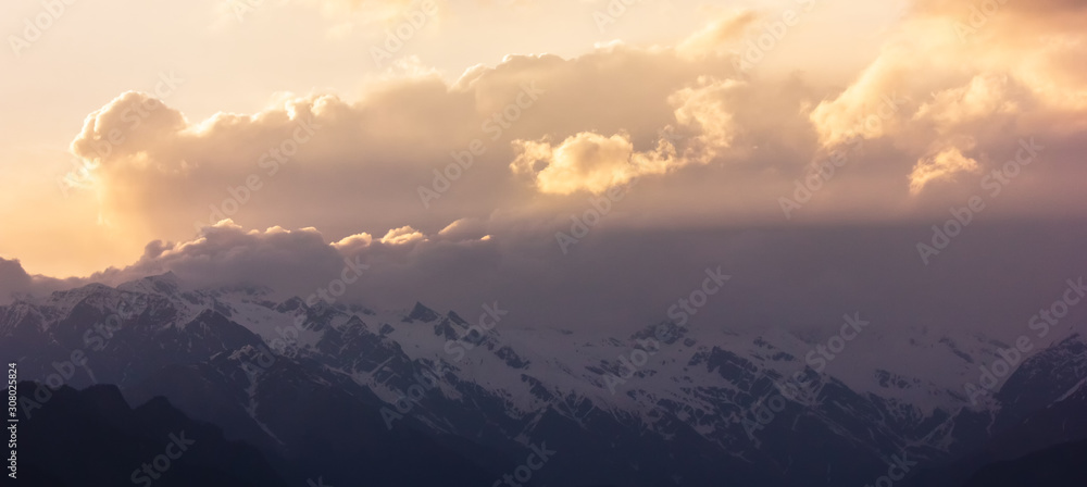 Obraz premium Sunlight streak through the clouds across the Shrikhand Mahadev range in the village of Sarahan in HImachal Pradesh, India. 
