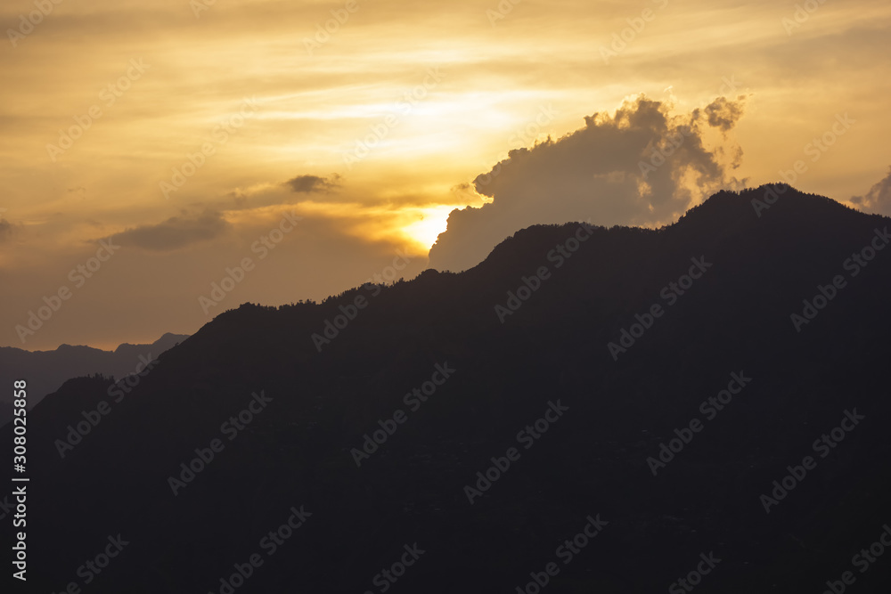 A view of a sunset behind a high mountain surrounding the village of Sarahan in Himachal Pradesh in the Indian Himalayas.