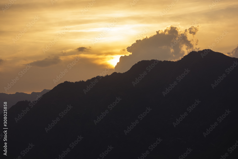 Obraz premium A view of a sunset behind a high mountain surrounding the village of Sarahan in Himachal Pradesh in the Indian Himalayas.