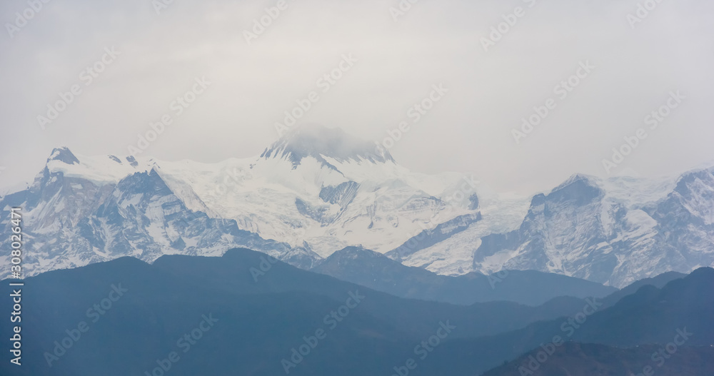 A view of the Annapurna range from the city of Pokhara in the dull, blue light of a misty morning.