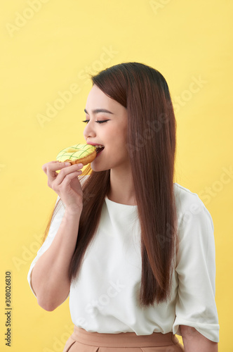 Close up portrait of a satisfied pretty girl eating donuts isolated over yellow background