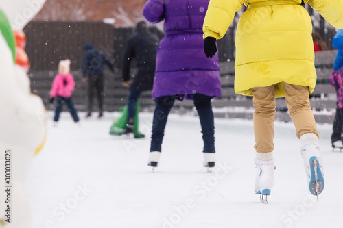 Girl in yellow jacket and woman in purple coat riding on an outdoor ice rink. Snow is falling. Leisure and recreation concept. Selective focus, blurred background, close up photo. Winter season.