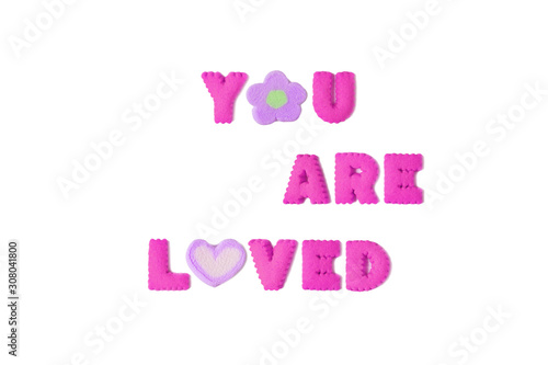 The word YOU ARE LOVED spelled with vivid pink alphabet cookies and purple marshmallow on white background
