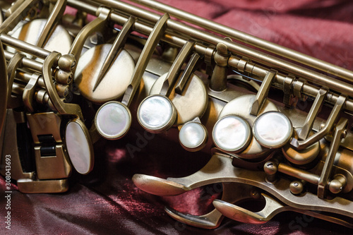 Part of a saxophone body. Close-up. Keys. Rose silk background.