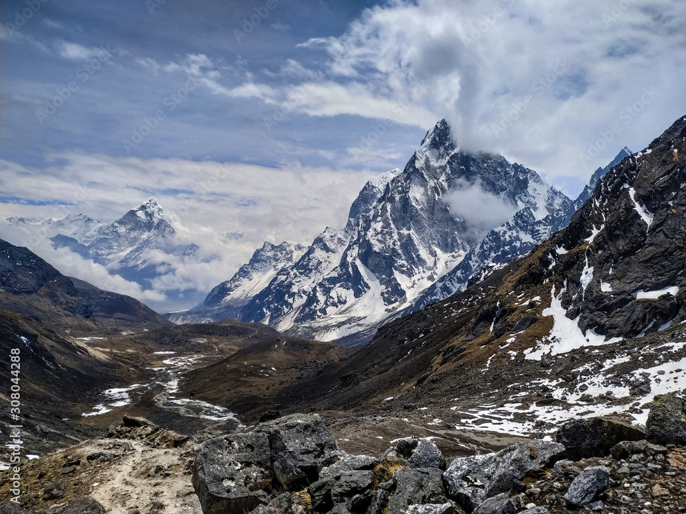 Cholatse and Taboche mountain peaks rises above valley near Cho La pass in Sagarmatha national park in Himalayas in cloudy day. Blurred Ama Dablam mountain is visible in the background.