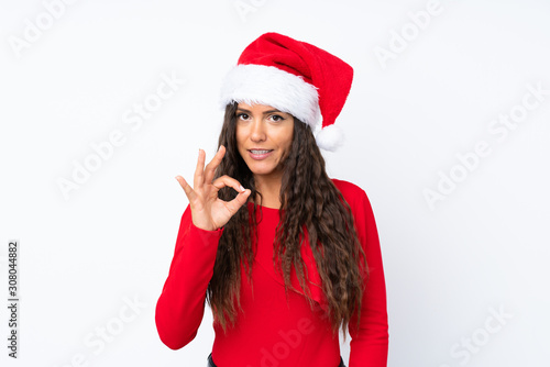 Girl with christmas hat over isolated white background showing an ok sign with fingers