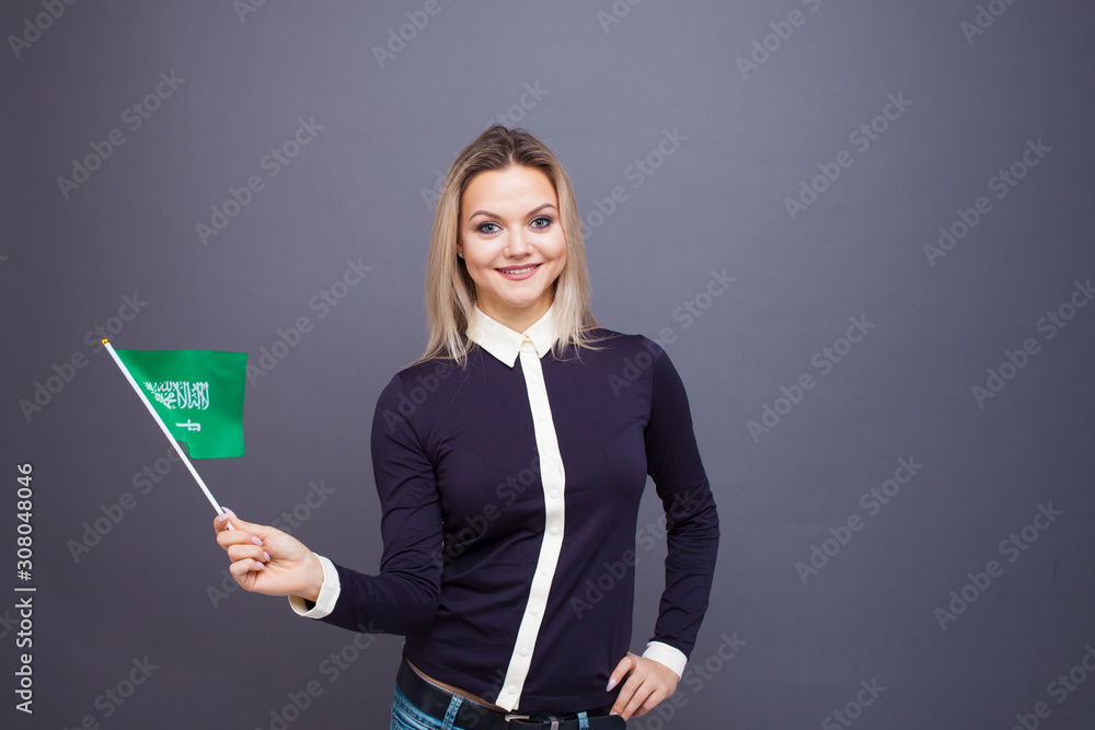 Immigration and the study of foreign languages, concept. A young smiling woman with a Saudi Arabia flag in her hand. Immigration and the study of foreign languages, concept. A young smiling woman with a Saudi Arabia flag in her hand.