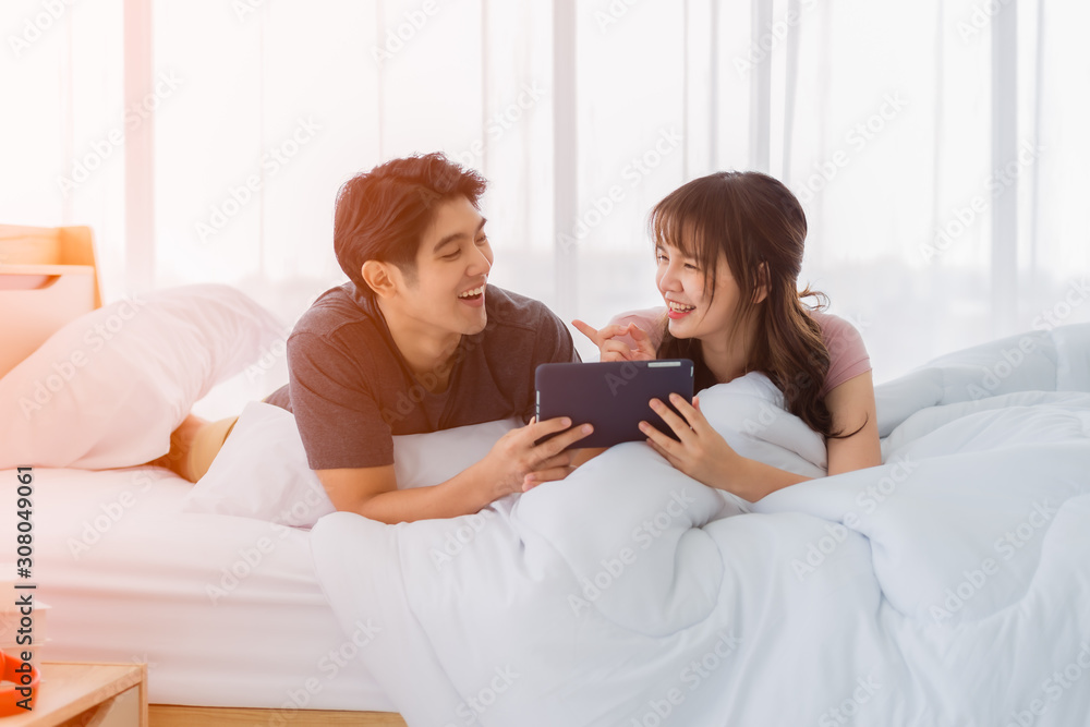 Asian couple is using smartphone surfing on the Internet on the bed in bedroom Asian couple is using smartphone surfing on the Internet on the bed in bedroom